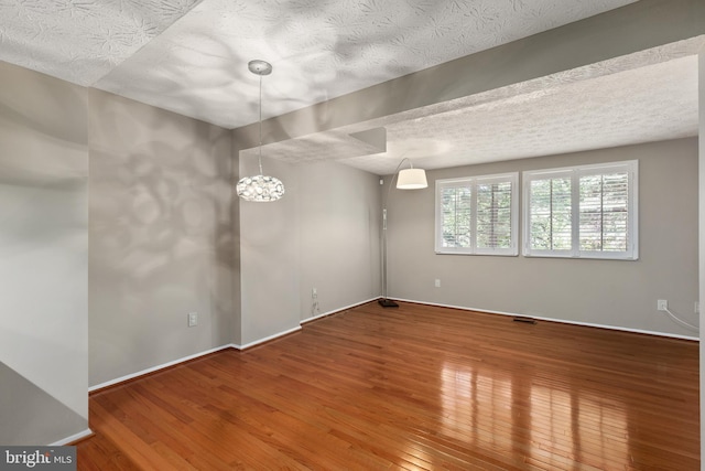 spare room featuring a textured ceiling, hardwood / wood-style floors, and a notable chandelier