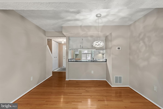 unfurnished dining area with a chandelier, visible vents, baseboards, a textured ceiling, and wood finished floors
