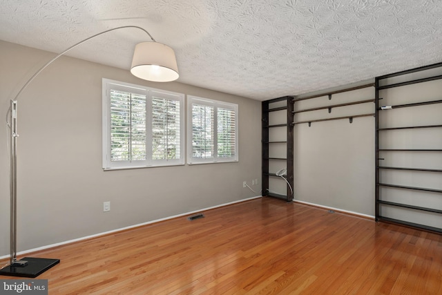 unfurnished bedroom featuring a textured ceiling, visible vents, wood finished floors, and baseboards