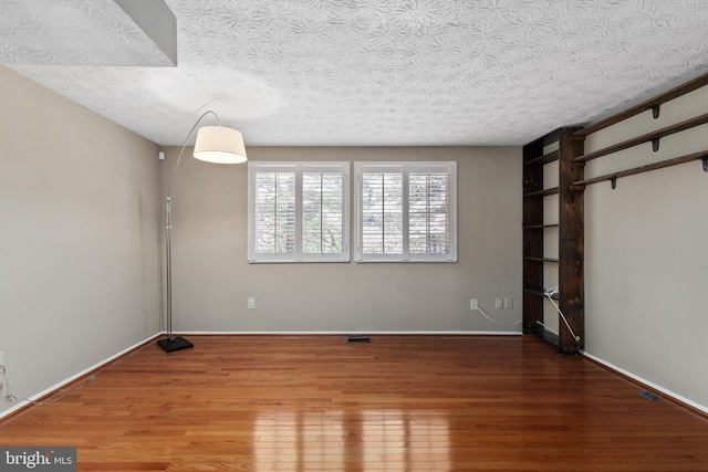spare room featuring a textured ceiling, wood finished floors, and baseboards