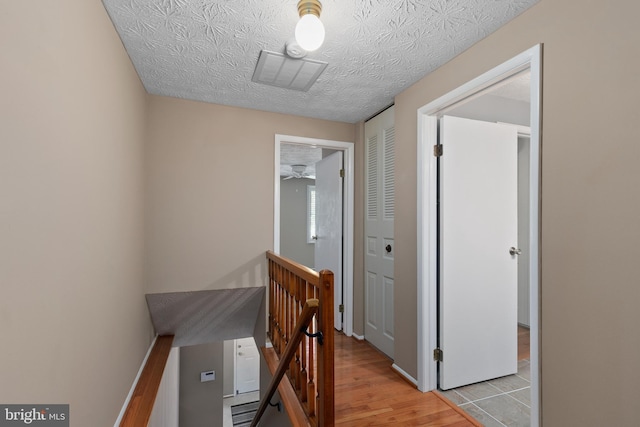 hall with an upstairs landing, visible vents, and light wood-type flooring