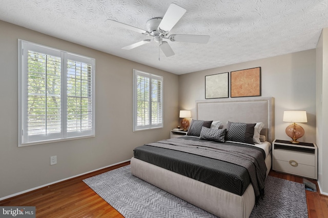 bedroom featuring a textured ceiling, ceiling fan, wood finished floors, and baseboards