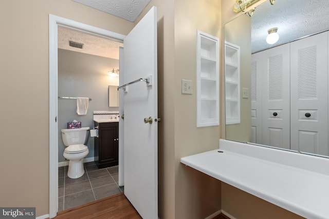 bathroom featuring a textured ceiling, visible vents, toilet, vanity, and tile patterned flooring