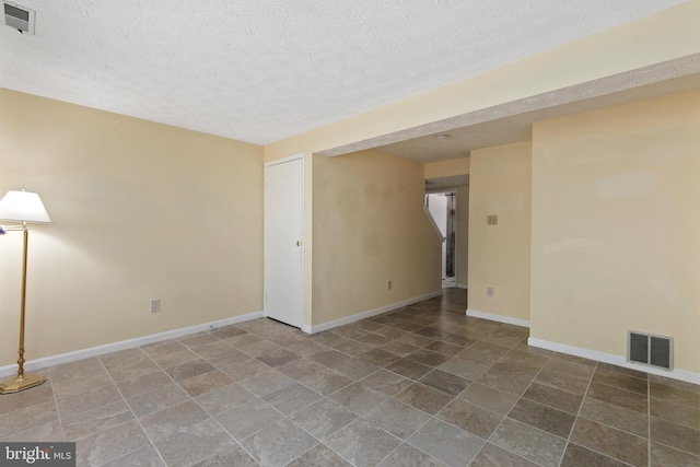 unfurnished room with a textured ceiling, visible vents, stone finish floor, and baseboards