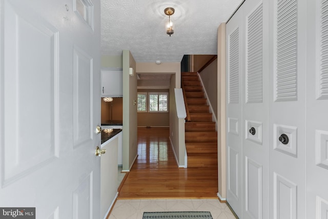 hall featuring light tile patterned floors, stairs, visible vents, baseboards, and a textured ceiling
