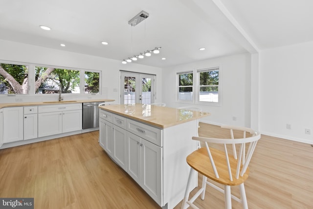 kitchen featuring stainless steel dishwasher, light wood-style floors, a kitchen bar, french doors, and a sink