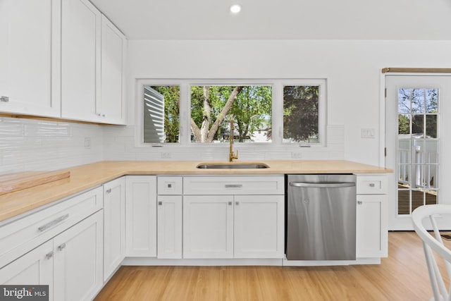 kitchen featuring a sink, light wood finished floors, light countertops, decorative backsplash, and stainless steel dishwasher