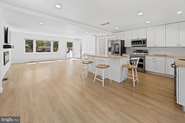kitchen with a kitchen breakfast bar, a kitchen island, appliances with stainless steel finishes, light countertops, and recessed lighting