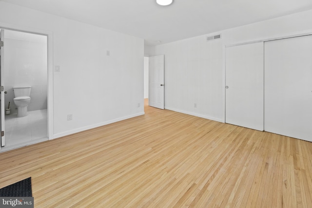 unfurnished bedroom featuring visible vents, a closet, wood finished floors, baseboards, and ensuite bath