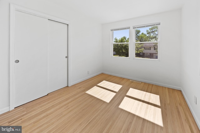 unfurnished bedroom featuring a closet, baseboards, wood finished floors, and visible vents