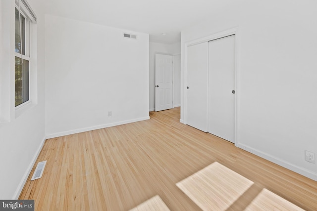 unfurnished bedroom with visible vents, baseboards, wood finished floors, and a closet