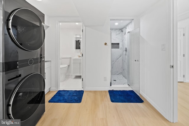 bathroom with stacked washing maching and dryer, a marble finish shower, baseboards, and wood finished floors