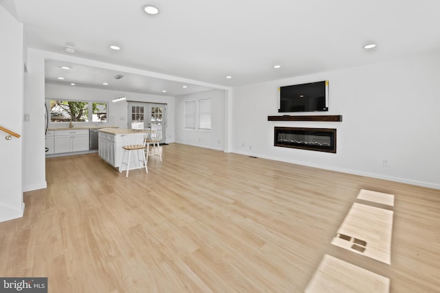 unfurnished living room with a glass covered fireplace, french doors, recessed lighting, and light wood-style flooring