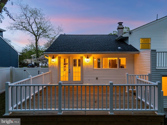 exterior space with french doors, a chimney, a wooden deck, fence, and a shingled roof