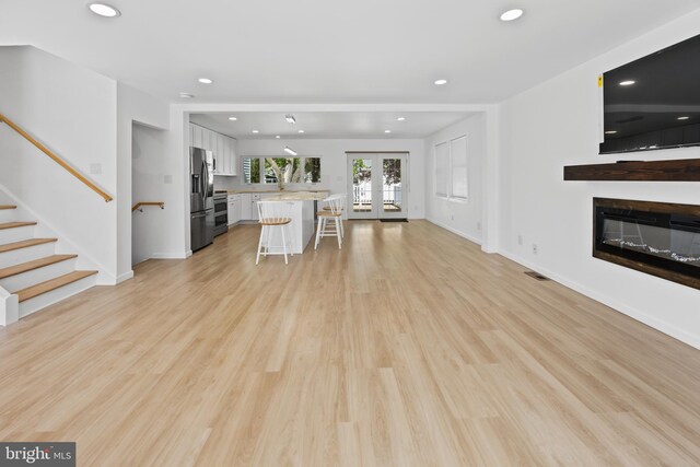 unfurnished living room featuring stairs, recessed lighting, a glass covered fireplace, and light wood-type flooring
