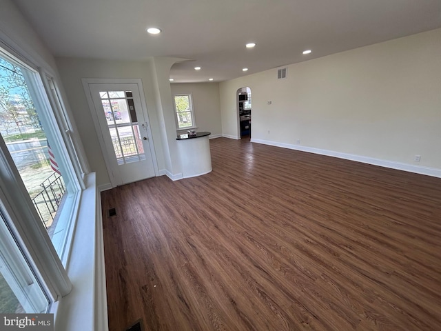unfurnished living room featuring visible vents, baseboards, dark wood-style floors, recessed lighting, and arched walkways