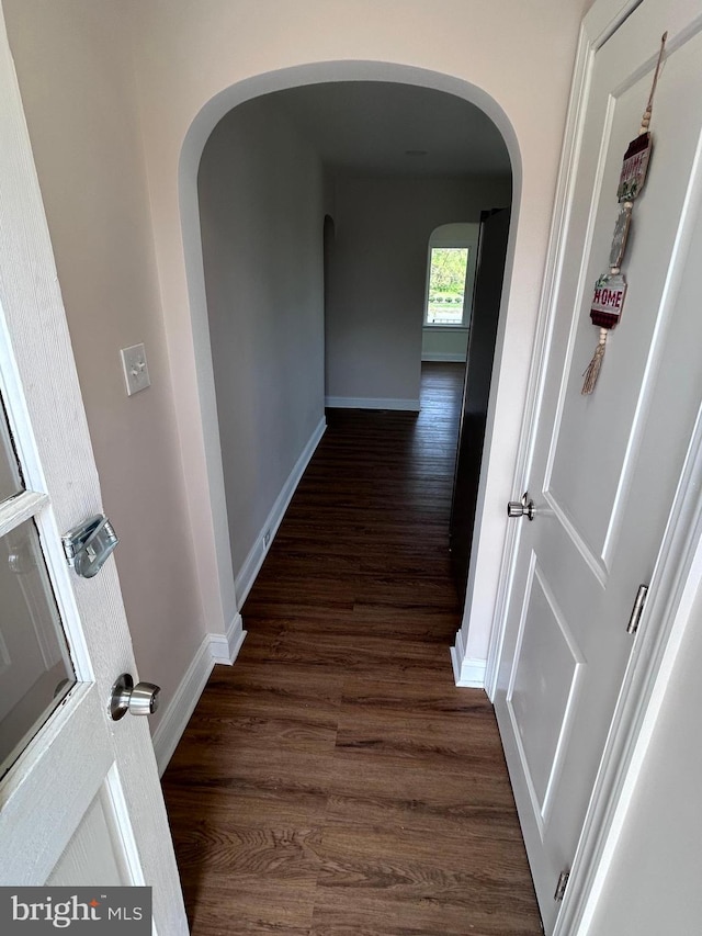 hallway featuring arched walkways, baseboards, and dark wood finished floors