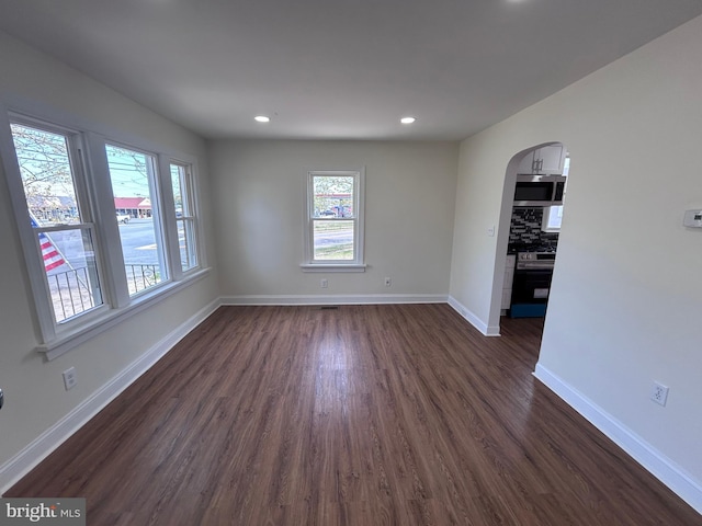 empty room featuring baseboards, arched walkways, dark wood finished floors, and recessed lighting