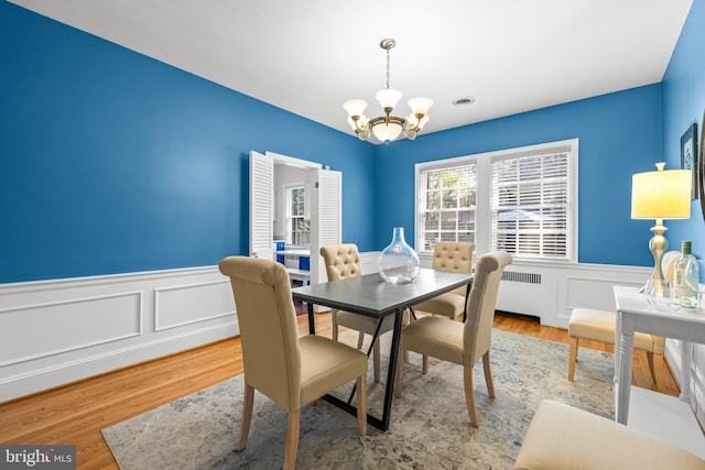 dining area featuring a decorative wall, a chandelier, wood finished floors, and a wainscoted wall