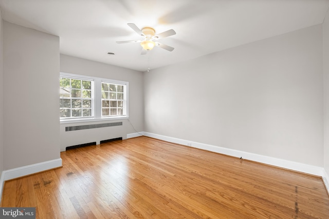 unfurnished room featuring radiator, a ceiling fan, baseboards, visible vents, and hardwood / wood-style flooring