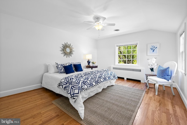 bedroom featuring visible vents, wood finished floors, baseboards, lofted ceiling, and radiator heating unit