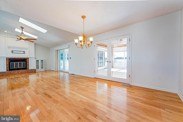 unfurnished living room with light wood-type flooring, a skylight, a brick fireplace, a ceiling fan, and a chandelier