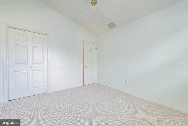 unfurnished bedroom featuring lofted ceiling, carpet floors, a closet, baseboards, and a textured ceiling