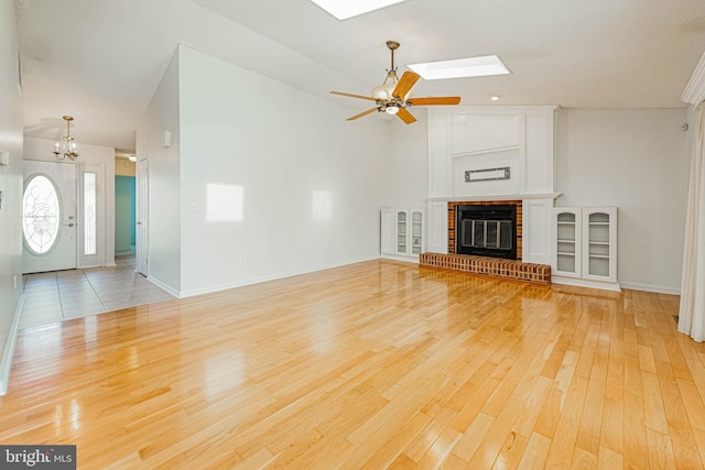 unfurnished living room featuring light wood-type flooring, a skylight, a chandelier, a fireplace, and a ceiling fan