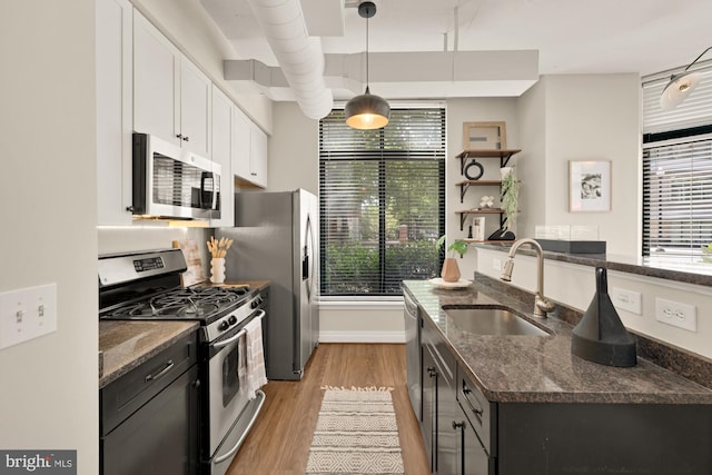 kitchen featuring white cabinets, a sink, light wood finished floors, dark stone counters, and stainless steel appliances