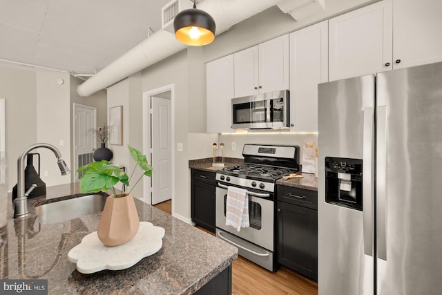 kitchen with a sink, dark stone countertops, appliances with stainless steel finishes, and light wood-style flooring