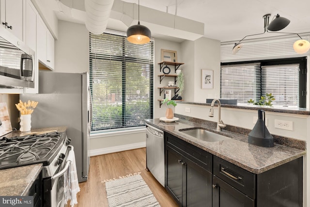 kitchen with appliances with stainless steel finishes, dark cabinets, a sink, light wood-style floors, and white cabinetry