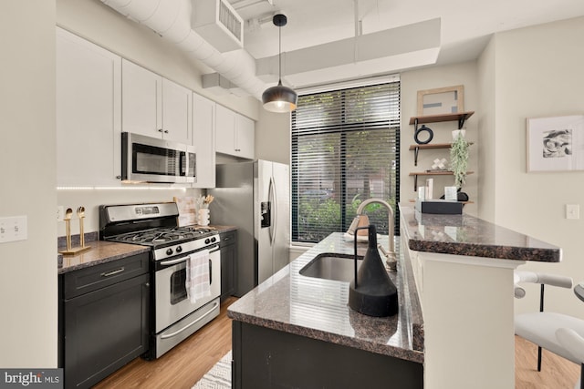 kitchen featuring a kitchen breakfast bar, dark stone counters, a sink, light wood finished floors, and stainless steel appliances