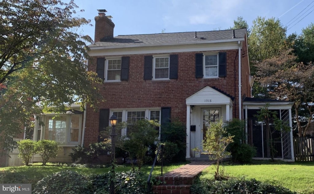 view of front facade featuring a chimney, brick siding, fence, and a front yard