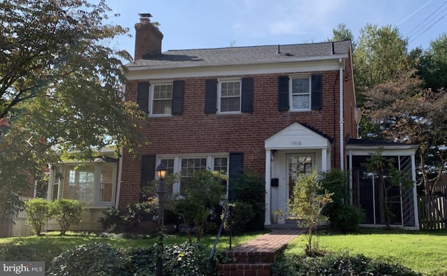 view of front facade featuring a chimney, brick siding, fence, and a front yard