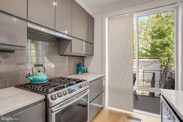 kitchen with light wood-style floors, stainless steel range with gas stovetop, gray cabinets, decorative backsplash, and visible vents