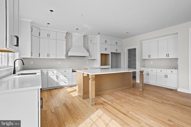 kitchen with a sink, light wood-type flooring, custom exhaust hood, a kitchen island, and white cabinets
