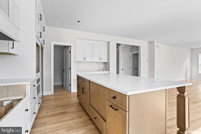 kitchen featuring light stone counters, white cabinetry, light wood-style flooring, a kitchen island, and baseboards