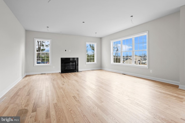 unfurnished living room featuring baseboards, a healthy amount of sunlight, a fireplace with flush hearth, and light wood-style floors