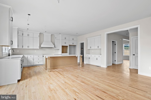 kitchen featuring custom exhaust hood, light wood-style floors, a kitchen island, a sink, and white cabinetry