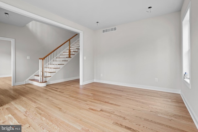 unfurnished living room featuring visible vents, stairway, light wood-style floors, and plenty of natural light