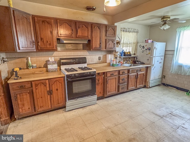 kitchen featuring freestanding refrigerator, brown cabinetry, light countertops, a sink, and range with gas cooktop