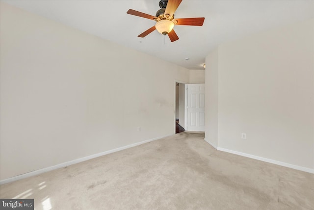 empty room featuring a ceiling fan, light colored carpet, and baseboards