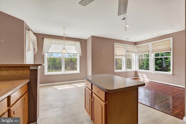 kitchen with pendant lighting, a kitchen island, baseboards, light wood-type flooring, and brown cabinetry