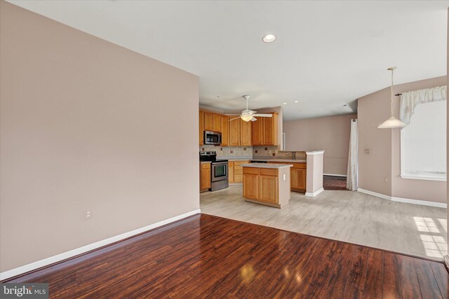 kitchen featuring light wood finished floors, stainless steel appliances, baseboards, a kitchen island, and light countertops