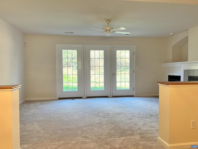 unfurnished living room with a wealth of natural light, visible vents, a ceiling fan, and carpet