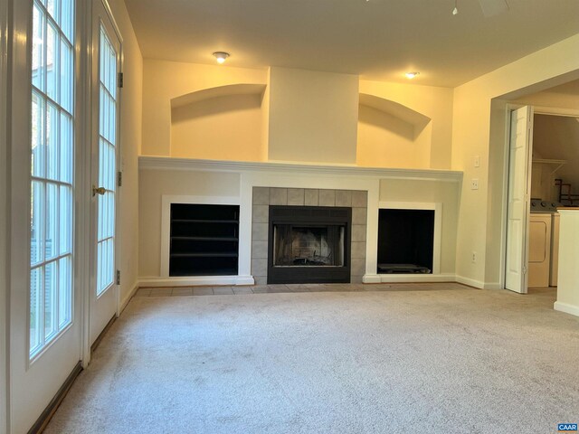 unfurnished living room featuring a tile fireplace, washer and clothes dryer, baseboards, and light carpet