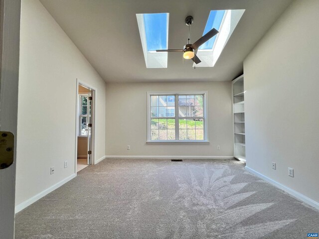interior space with lofted ceiling with skylight, visible vents, carpet flooring, and baseboards