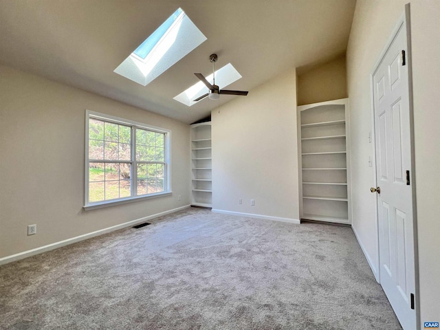 interior space featuring visible vents, carpet floors, baseboards, a ceiling fan, and a skylight
