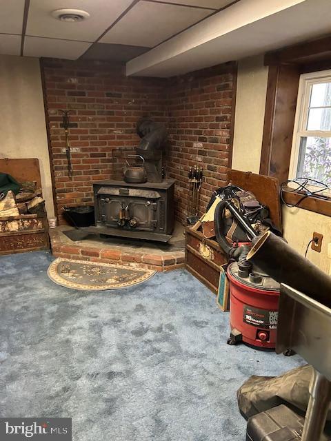 living room with carpet floors, visible vents, a paneled ceiling, and a wood stove