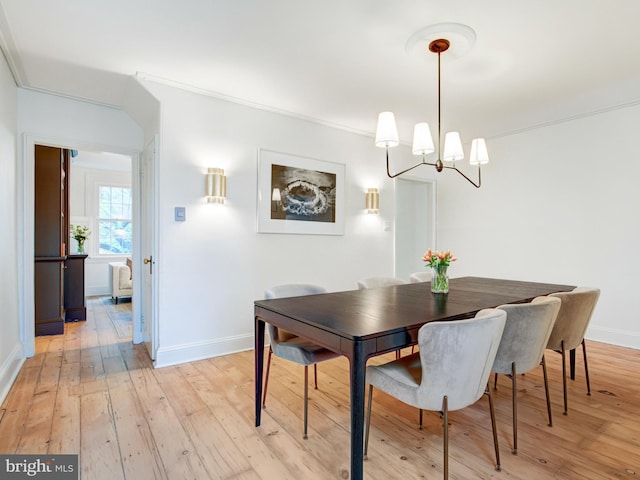 dining space with baseboards, ornamental molding, light wood-type flooring, and a notable chandelier